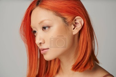 retrato de delicada joven mujer asiática con la piel perfecta y el pelo rojo posando sobre fondo gris