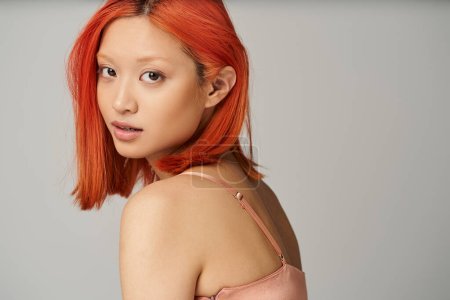 verführerische junge asiatische Frau mit perfekter Haut und natürlichem Make-up vor der Kamera auf grauem Hintergrund