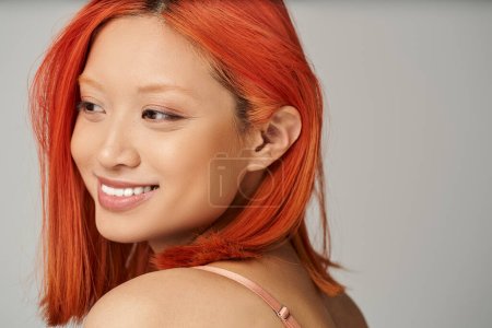 charming young asian woman with perfect skin and natural makeup smiling on grey background
