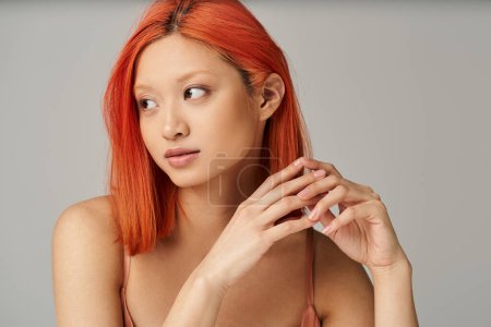 Téléchargez les photos : Rêveuse jeune femme asiatique avec peau parfaite et maquillage naturel regardant loin sur fond gris - en image libre de droit