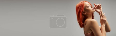 dreamy asian woman with closed eyes standing in slip dress on grey background, feminine grace banner