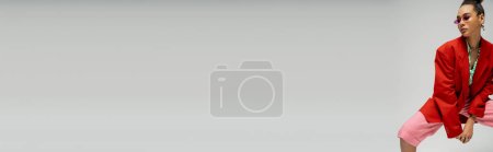 Téléchargez les photos : Jeune femme afro-américaine en lunettes de soleil et tenue tendance posant sur fond gris, bannière - en image libre de droit