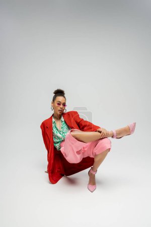 full length, african american model in modern attire and pink high heels posing on grey backdrop
