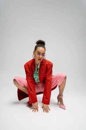 Persönlicher Stil, afrikanisch-amerikanische Frau in moderner Kleidung und rosa High Heels posiert vor grauem Hintergrund
