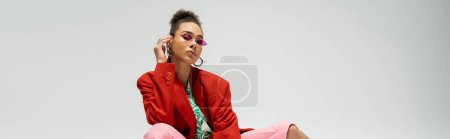 african american fashion model in stylish attire and sunglasses posing on grey backdrop, banner