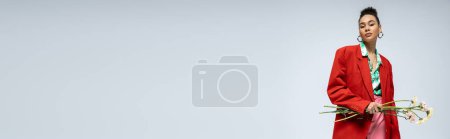 Téléchargez les photos : Jolie femme américaine africaine en blazer rouge tenant des fleurs et regardant la caméra sur bannière grise - en image libre de droit