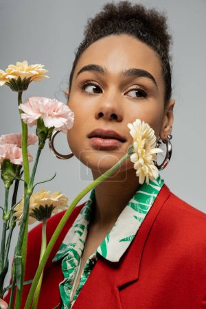 close up portrait of african american woman in red blazer holding flowers on grey backdrop