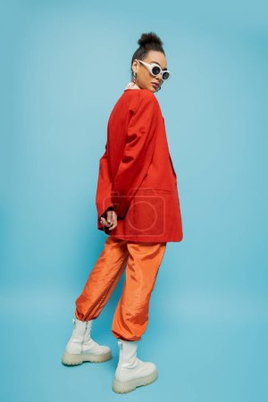 persönlicher Stil, junges afrikanisch-amerikanisches Model in lebendigem Outfit posiert auf blauem Hintergrund