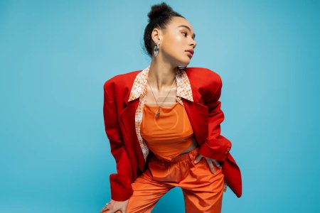 stylish african american model in bold colourful attire and hoop earrings posing on blue background