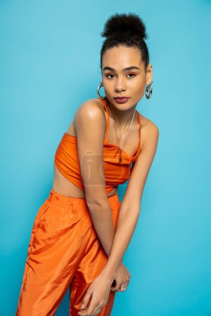 stylish african american model in striking orange outfit with golden accessories looking at camera