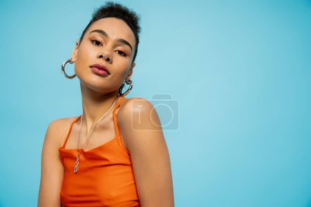 portrait of young african american model in vivid clothing and bright makeup on blue backdrop