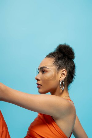 Téléchargez les photos : Portrait de jeune femme afro-américaine posant de profil, portant une tenue orange et des boucles d'oreilles cerceau - en image libre de droit