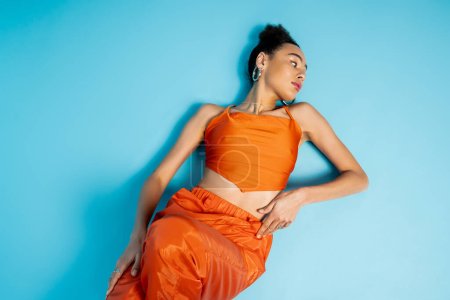 stylish attractive woman posing on floor wearing catchy bright attire and hoop earrings looking away