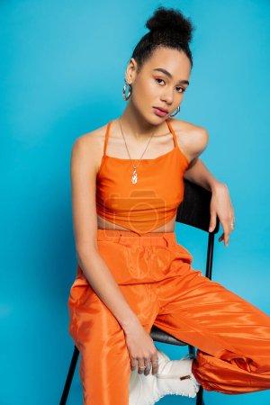 Nahaufnahme Mode-Modell in orange stilvolle Kleidung und lebhaftes Make-up sitzen und in die Kamera schauen