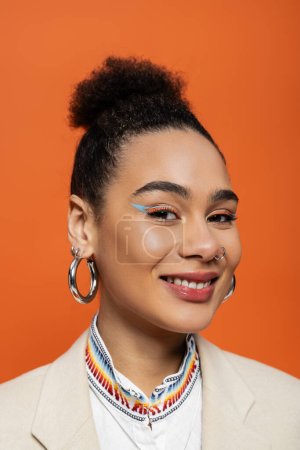 portrait of cheerful african american model with bright make up and hoop earrings smiling at camera