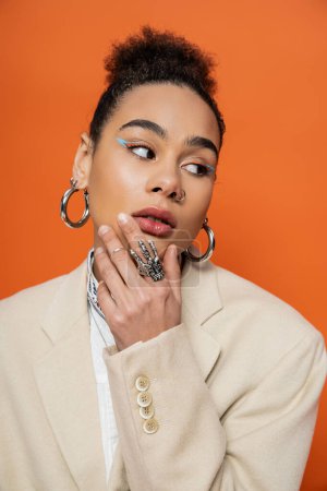 portrait of attractive young model with bright makeup, hoop earrings and silver rings, hand to face