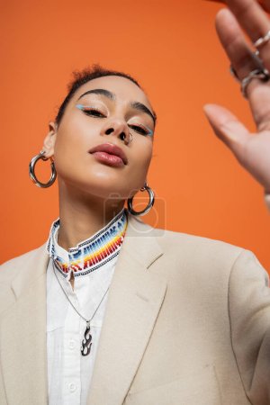 Téléchargez les photos : Fermer modèle afro-américain à la mode avec maquillage coloré et boucles d'oreilles cerceau regardant la caméra - en image libre de droit