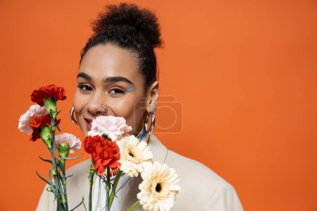portrait of cheerful fashion model with vibrant colourful makeup and bun posing with flower bouquet