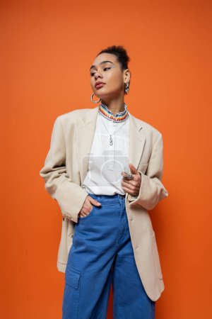 Foto de Atractivo modelo afroamericano en elegante traje urbano y anillos de plata sobre fondo naranja - Imagen libre de derechos