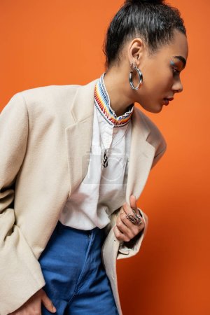 attractive fashion model in beige blazer hoop earrings and silver rings on orange background