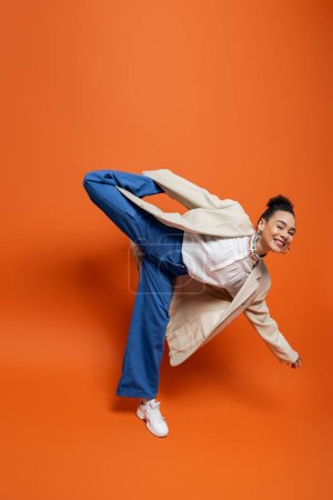 lustiges afrikanisch-amerikanisches Model in stylischem urbanem Outfit mit verspielt erhobenem Bein auf dem Rücken