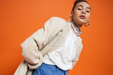 pretty african american woman in beige blazer with colourful collar hoop earrings and vivid makeup