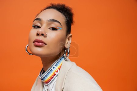 Porträt eines trendigen afrikanisch-amerikanischen Models in schicker Kleidung mit farbenfrohem Make-up, das in die Kamera blickt