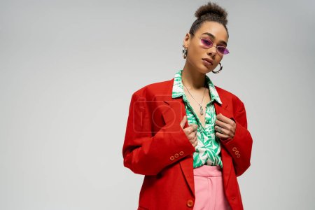 stylisches afrikanisch-amerikanisches Model in trendiger Sonnenbrille und trendiger, lebendiger Kleidung vor grauem Hintergrund