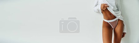 Photo for Cropped slim woman with pierced belly standing in panties and sweater on white backdrop, banner - Royalty Free Image
