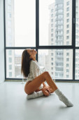 young woman in socks and long sleeve shirt sitting on floor at home, posing near panoramic window hoodie #674382996