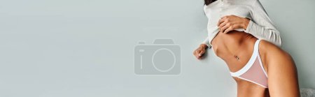 Photo for Cropped view of passionate woman with pierced belly lying on floor, panties and long sleeve, banner - Royalty Free Image