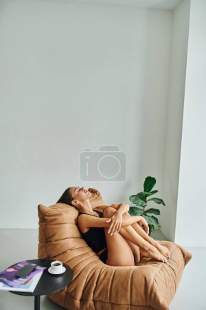 atractiva mujer descalza descansando en la silla de la bolsa de frijol cerca de la mesa de café con taza de café negro