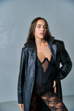 mujer sexy con el pelo mojado morena posando en abrigo de cuero negro y ropa interior de encaje, mano en la cadera