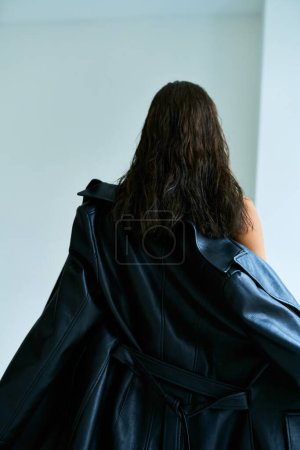 back view of stylish woman with brunette hair standing in black leather coat, fashionable model
