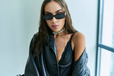 Foto de Retrato de mujer seductora en gafas de sol posando en ropa interior de encaje negro y abrigo de cuero - Imagen libre de derechos