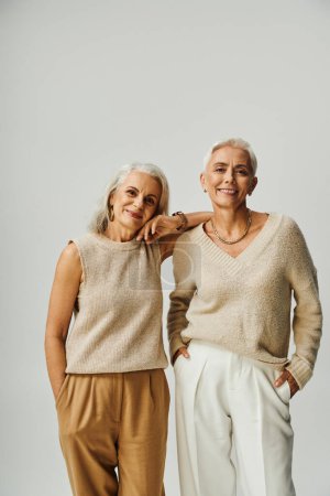Smiley-Seniorinnen in stylischer Pastellkleidung blicken in die Kamera auf Grau, Positivität und Charme