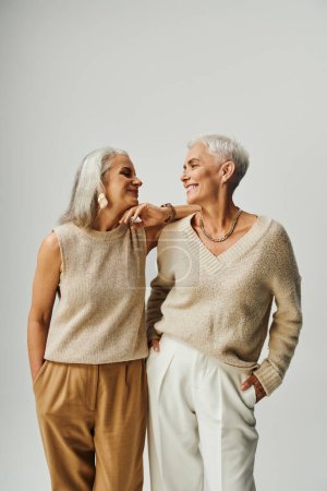 trendige Seniorinnen in pastellfarbener Kleidung, die sich auf grauen, modischen Langzeit-Freundinnen anschauen