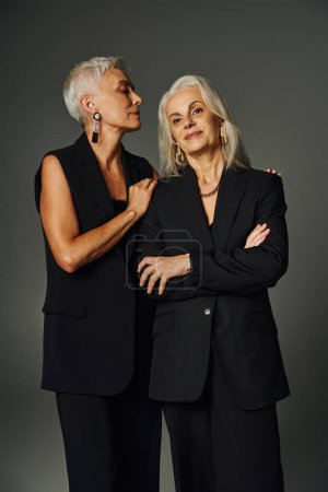 Téléchargez les photos : Élégante femme âgée avec les bras croisés près d'amie sur le vieillissement gris, gracieux et positif - en image libre de droit