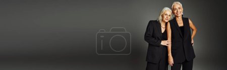 Téléchargez les photos : Souriant mature dames en noir vêtements à la mode en regardant la caméra sur gris, amitié à vie, bannière - en image libre de droit
