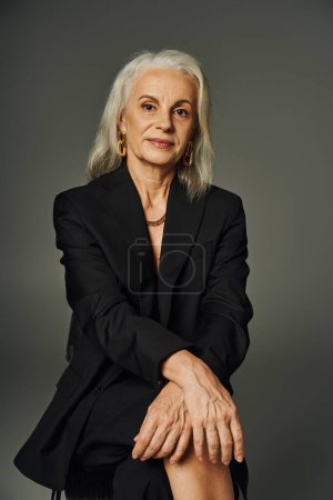 ältere weibliche Modell in schwarzer eleganter Kleidung sitzt und blickt ta Kamera auf graue, anmutige Alterung