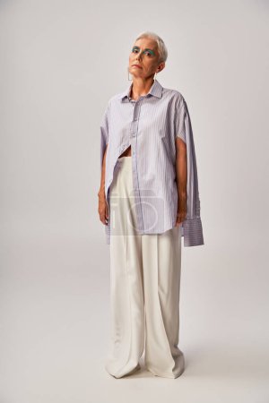 full length of fashionable mature lady in blue striped short and white pants on grey backdrop