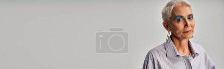 Téléchargez les photos : Portrait de dame âgée aux cheveux courts argentés et au maquillage audacieux souriant à la caméra sur gris, bannière - en image libre de droit