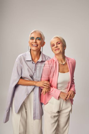 positive senior female friends in stylish casual attire smiling on grey, happy and trendy aging