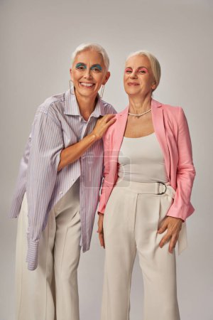 gaies dames âgées en tenue décontractée à la mode souriant à la caméra sur gris, vieillissement heureux