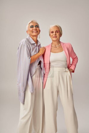 joyful senior ladies in fashionable casual attire looking at camera on grey, happy aging concept