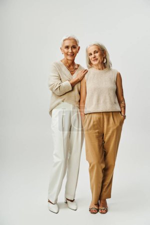 Foto de Longitud completa de felices amigas mayores en ropa pastel de moda de pie sobre fondo gris - Imagen libre de derechos
