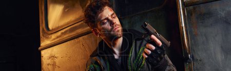 hombre con la cara herida mirando el arma en el metro abandonado, sobreviviente post-apocalíptico, pancarta