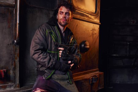 survived injured man holding gun and looking away in abandoned subway, post-apocalyptic concept
