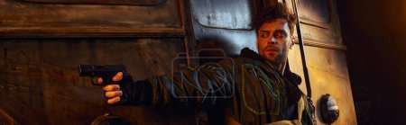 Photo for Unshaven game character in worn clothes aiming with gun in dangerous post-apocalyptic subway, banner - Royalty Free Image