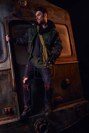 Mann in abgetragener Kleidung steht mit Waffe auf rostigem Wagen in dunkler U-Bahn, postapokalyptische Dystopie
